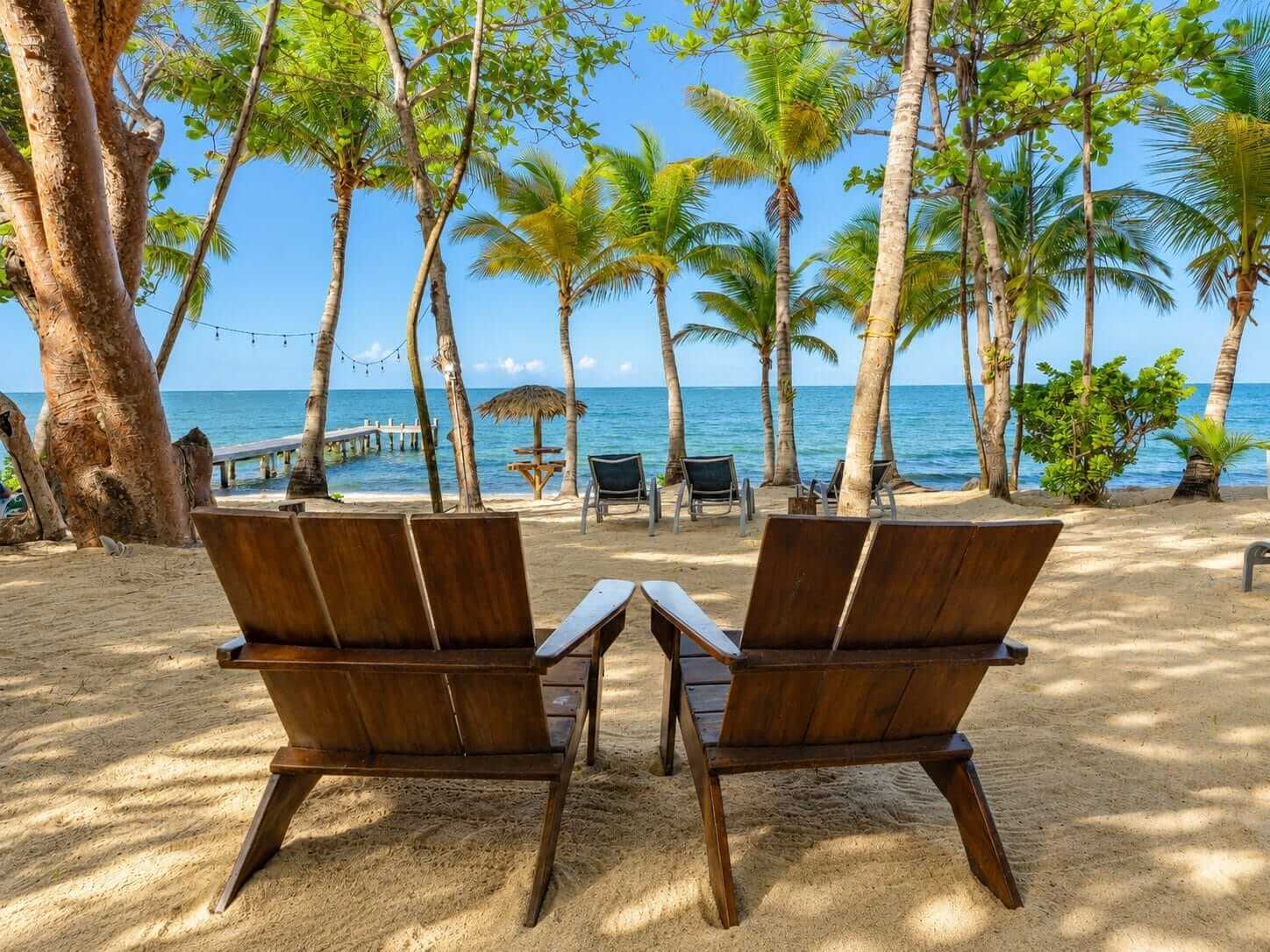 Two Adirondack chairs on the sand facing the sea