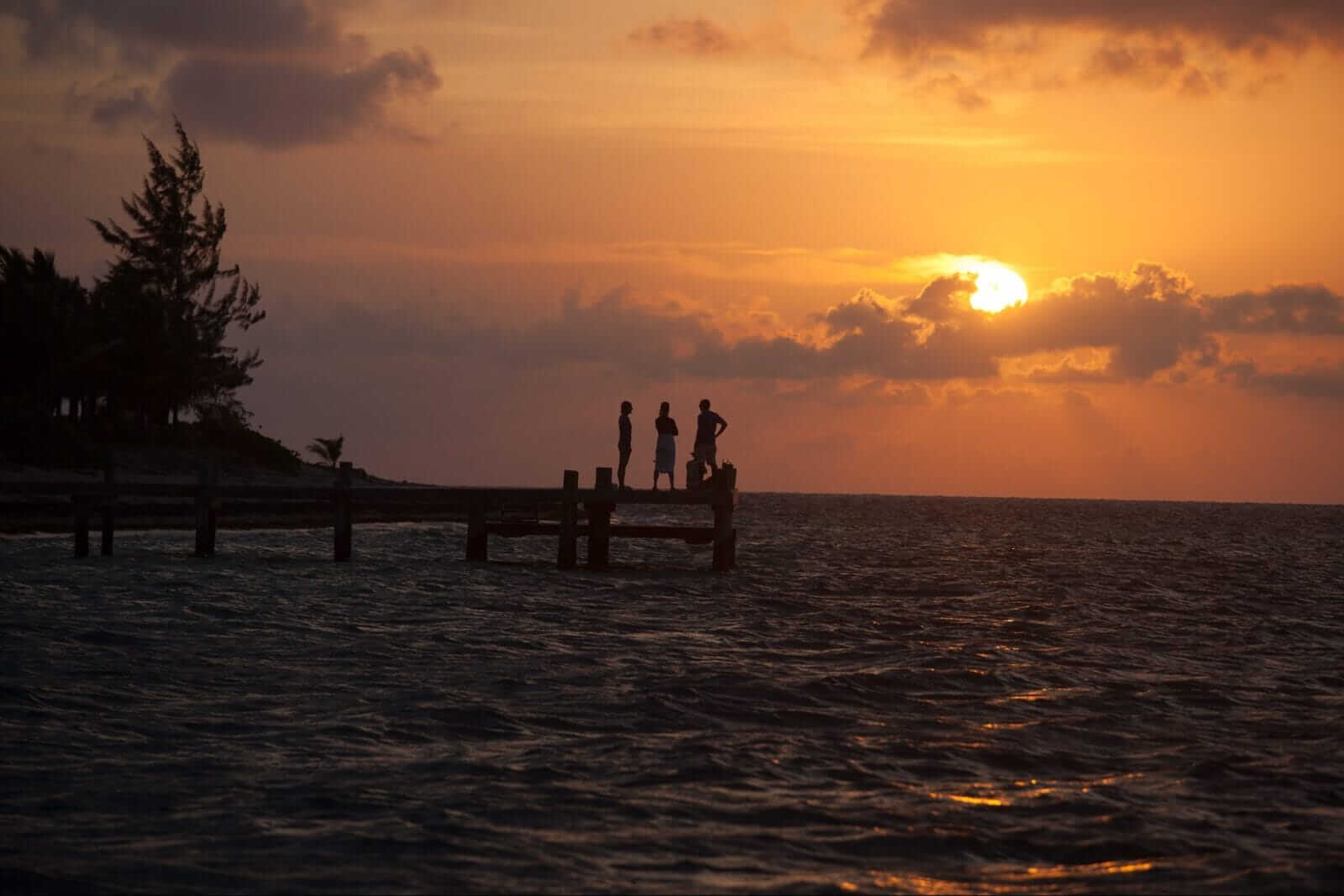Figures on the dock at sunset over the Caribbean