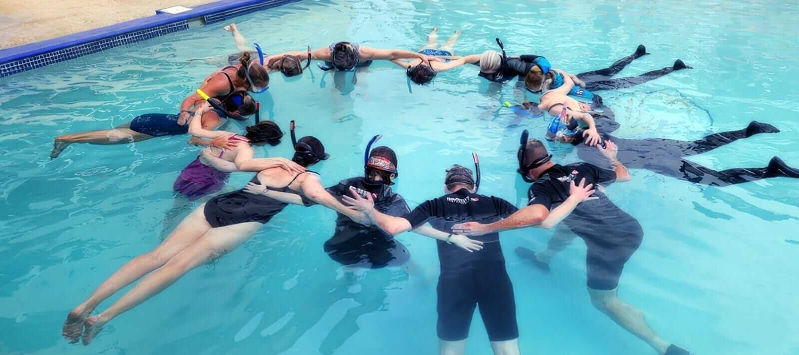 The group floating in a circle in the pool, joined hand to hand in snorkel gear
