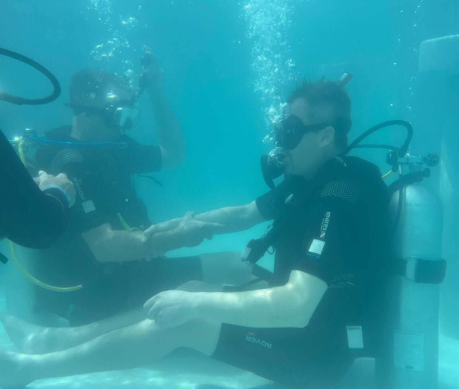 A retreat guest held by a dive professional during an underwater meditation
